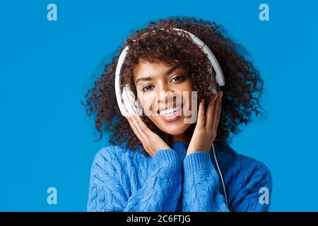 Close-up portrait hipster attractive african-american woman with curly hairstyle, put on headphones and smiling, enjoying music, listen to favorite Stock Photo