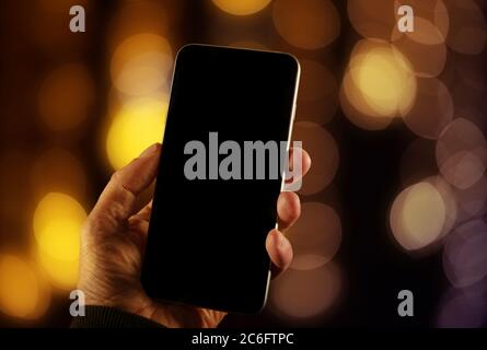 Close up view of a man using empty screen smartphone with background defocused warm colored lights Stock Photo