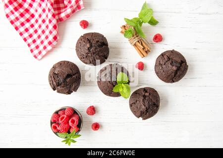 Chocolate muffins with raspberries and mint leaves on white wooden background, top view Stock Photo
