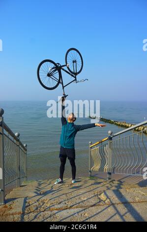 Baltic sea, Kaliningrad region, Russia, March 28, 2020. Young man lifts a Bicycle. A young man on the sea with a Bicycle. Stock Photo