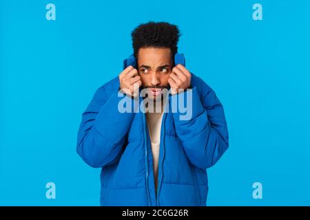 Embarrassed or ashamed guy hiding his face not to be recognized in public. Nervous and alarmed african american man pull collar of padded jacket on Stock Photo
