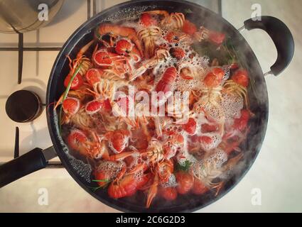 Cooking river crayfish, or crawfish, at home on a traditional recipe. A lot of red, freshwater lobsters boiling in a big bowl on hob. Preparing delici Stock Photo