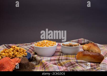 Close up of typical June Party foods on a wooden table: Popcorn, cornmeal cake, corn kernels, peanut pods and small country hats. Copy space. Selectiv Stock Photo