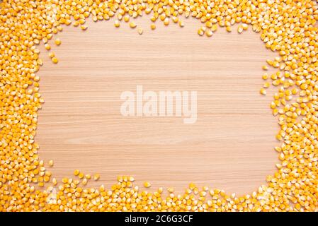 Frame created by grains of raw corn on wood. White space for text, figures or icons. Raw corn kernels for popcorn frame and border isolated on white b Stock Photo