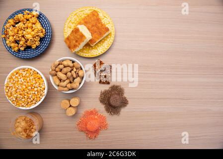 Top view of typical June Party foods on a wooden table: Popcorn, cornmeal cake, corn kernels, peanut pods, peanuts candies (paçoca) and dulce de leche Stock Photo