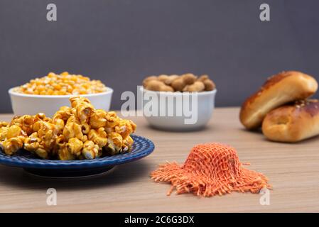 Close up of typical June Party foods on a wooden table: Popcorn, cornmeal cake, corn kernels, peanut pods and small country hats. Copy space. Selectiv Stock Photo