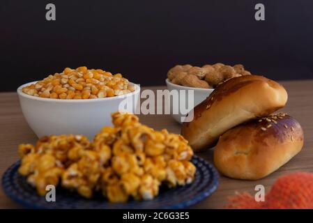 Close up of typical June Party foods on a wooden table: Popcorn, cornmeal cake, corn kernels, peanut pods and small country hats. Copy space. Selectiv Stock Photo