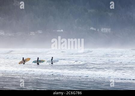 Three young men headed out into the suf with surfboards. Pacific coast, Seaside, Oregon, USA. Stock Photo