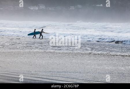 Two young men headed out into the suf with surfboards. Pacific coast, Seaside, Oregon, USA. Stock Photo