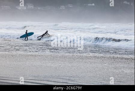 Two young men headed out into the suf with surfboards. Pacific coast, Seaside, Oregon, USA. Stock Photo