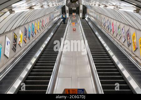 LONDON, ENGLAND - JUNE 8, 2020:  London Underground escalator with a young Afro-Caribbean woman wearing a face mask observing social distancing measur