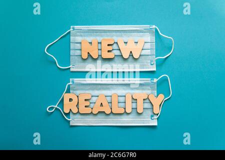 NEW REALITY words on protective face masks on blue background. Post covid-19 pandemic changes, new normal, wearing face mask in public concept. Stock Photo