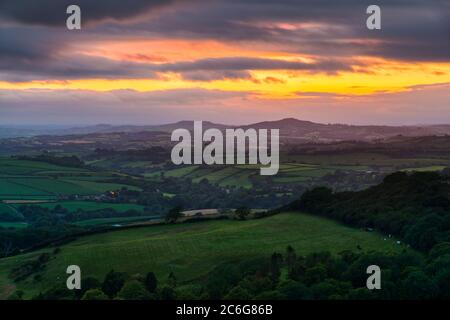 Askerswell, Dorset, UK.  9th July 2020.  UK Weather.  View from Eggardon Hill near Askerswell in Dorset looking towards the hills of Pilsdon Pen and Lewesdon Hill as a break in the dark moody clouds glow orange at sunset.  Picture Credit: Graham Hunt/Alamy Live News Stock Photo