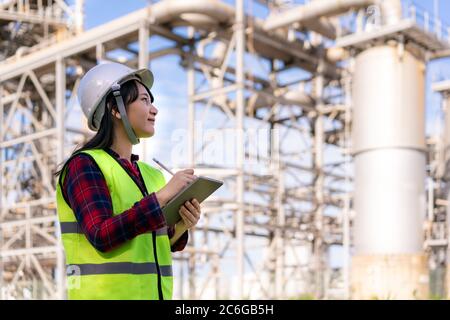 Asian woman petrochemical engineer working with digital tablet Inside oil and gas refinery plant industry factory for inspector safety quality control Stock Photo