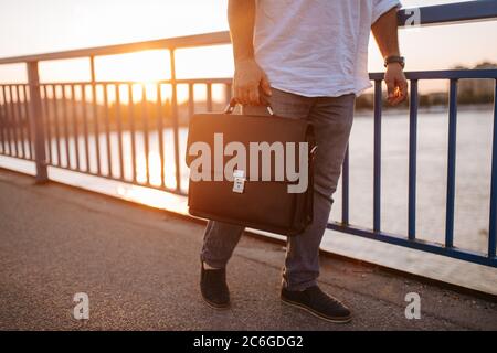 Closeup of black briefcase carried in the hand of a middle-aged businessman on a bridge Stock Photo