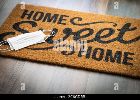 Medical Face Masks Rests on Home Sweet Home Welcome Mat Amidst The Coronavirus Pandemic. Stock Photo