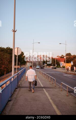 A middle-aged caucasian businessman with glasses, in a white shirt and a black briefcase in his hand walks on the bridge Stock Photo
