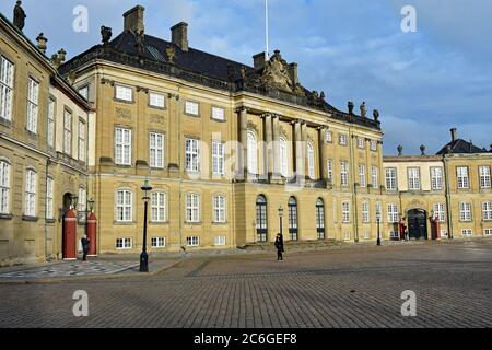 Amalienborg Palace in Copenhagen, Denmark. One tourist takes a photo of the palace and another is walking past. The Guard boxes and lamps are visible. Stock Photo