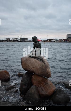 The Little Mermaid Statue in Copenhagen Harbour from the Langelinie Promenade.  The Bronze Mermaid is sat looking out to sea on a pile of rocks.