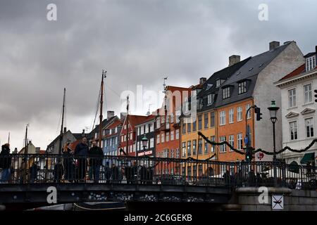 The colourful townhouses on the northern side of Nyhavn Canal are seen behind the Nyhavn bridge. Visitors can be seen walking across the bridge. Stock Photo
