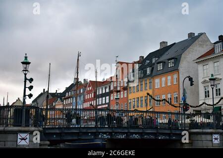 The colourful townhouses on the northern side of Nyhavn Canal are seen behind the Nyhavn bridge. Visitors can be seen enjoying the view on the bridge. Stock Photo