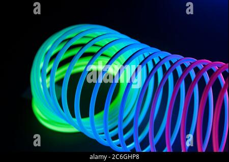 Multi-colored circular spiral objects are viewed in close and lit with fluorescent colors against a deep blue background. Stock Photo