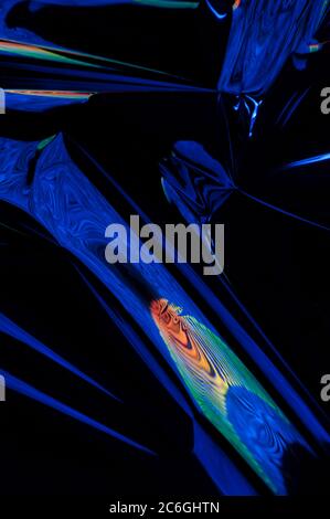 Circular objects which are distorted are viewed in a close-up and are lit with fluorescent colors against a deep blue background. Stock Photo
