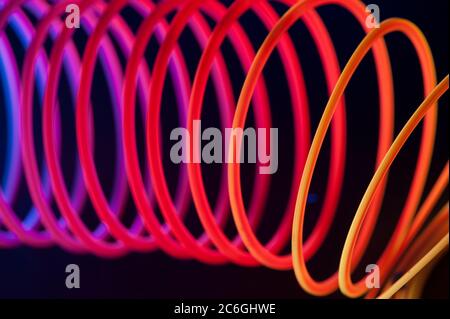 Red circular spiral objects are viewed in close and lit with fluorescent colors against a deep blue background. Stock Photo