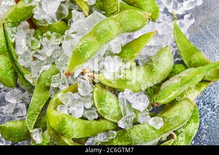 Frozen Edamame or soybeans in the mix with crushed ice on a blue background. Stock Photo