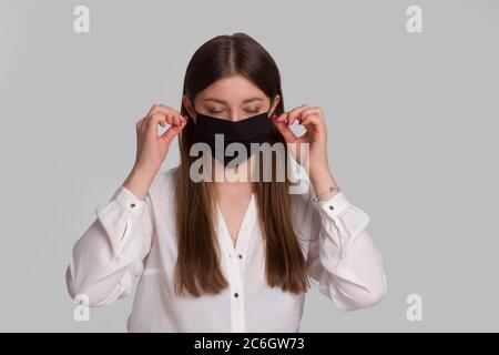 A young woman wears a black protective mask. Isolated on gray. The concept of a viral epidemic. Stock Photo