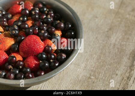 Strawberries and black currants in bowl on wood table in sunny summer day Stock Photo