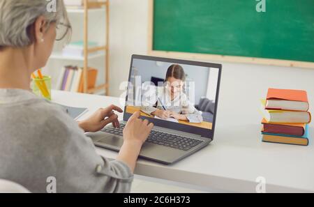 Online teacher teaches a child. Little girl writes a lecture lesson in a notebook using a video chat with a laptop teacher remotely at home. Stock Photo