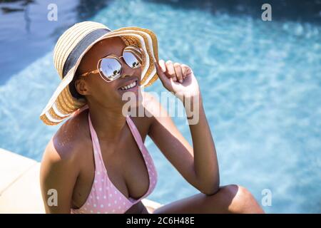 Woman wearing hat and sunglasses while sitting by the pool Stock Photo