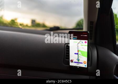 Using waze maps application on smartphone on car dashboard, Driver using maps app for showing the right route through the traffic of city at sunset on Stock Photo