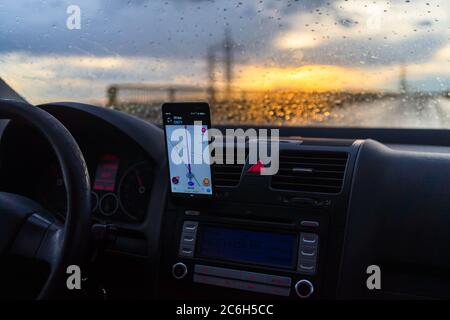 Using waze maps application on smartphone on car dashboard, Driver using maps app for showing the right route through the traffic of city at sunset on Stock Photo