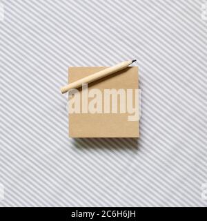 Brown kraft memo pad, empty paper with wooden pencil on gray stripe pattern fabric background. top view, copy space Stock Photo