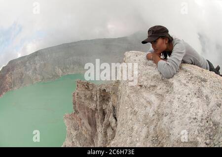 Woman tourist looking at turquoise-green coloured lake and side of crater, Mount Ijen, East Java, Indonesia, Asia Stock Photo