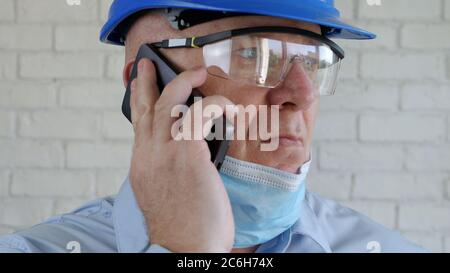 Engineer with Safety Helmet and a Protection Mask on His Face Talking to the Cell Phone Stock Photo