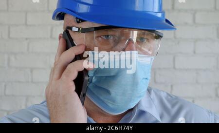 Engineer with Safety Helmet and a Protection Mask on His Face Talking to the Cell Phone Stock Photo