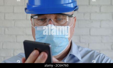 Engineer with Safety Helmet and a Protection Mask on His Face Talking to the Cell Phone Stock Photo