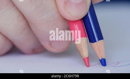 Image with a Person Drawing with Two Colored Pencils on a White Piece of Paper Stock Photo
