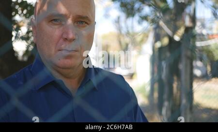 Portrait of a Man Behind a Metal Fence Standing Isolated from the Rest of the People Stock Photo