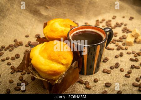 Two fresh cupcakes, a coffee mug, and coffee beans on a rough-textured homespun fabric. Close up Stock Photo