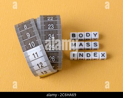 Measuring tape with centimeters and Body Mass Index words made of white cubes on a yellow background. Concept of healthy eating, dieting, weight loss. Stock Photo