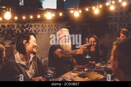 Happy family dining and tasting red wine glasses in barbecue dinner party - People with different ages and ethnicity having fun together Stock Photo