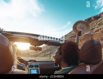 Young women doing road trip in tropical city - Travel happy people having fun driving in trendy convertible car discovering new places