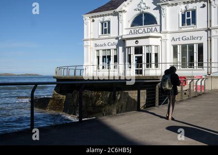 Person walks past the beautiful white fronted Arcadia beach cafe and art gallery along the shoreline at Portrush, Co. Antrim, Northern Ireland Stock Photo