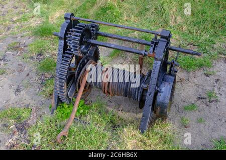 Old black winch with rusting cables, heavy vintage machinery lying on the grass at Portmuck Harbour on Islandmagee in Northern Ireland Stock Photo