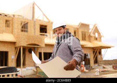 Bearded builder holding architectural drawing plan on paper at construction site. Stock Photo