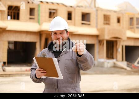 Caucasian foreman giving apartment keys and holding drawing plan in notebook. Stock Photo